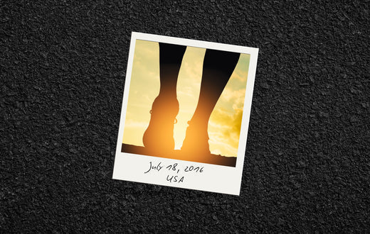 A polaroid photograph lying on an asphalt surface, showing the silhouette of a person’s legs and running shoes against a vibrant sunset. The bottom of the polaroid has handwritten text that reads 'July 18, 2016, USA.